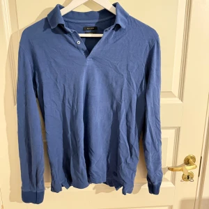 Blå långärmad pikétröja Massimo Dutti - Snygg blå långärmad pikétröja från Massimo Dutti med klassisk krage och knappslå. Tröjan har en avslappnad passform och är tillverkad i ett mjukt material som känns skönt mot huden. Perfekt för en stilren och enkel look. Passar S