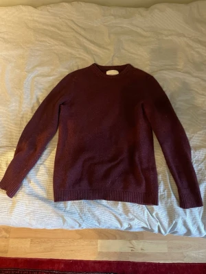 Vinröd tröja med mockadetaljer - Mysig vinröd stickad tröja med rund halsringning och ribbade muddar. Tröjan har snygga ljusbruna mockalappar på armbågarna som ger en cool touch. Perfekt för dig som gillar klassisk men trendig stil.