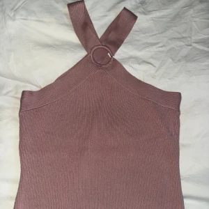 Rosa ribbad linnetopp med ringdetalj XS-S - Trendig rosa ribbad linnetopp med breda axelband som korsas i ryggen och en snygg ringdetalj framtill. Toppen är croppad och har en figurnära passform, perfekt till jeans eller kjol. Materialet är mjukt och stretchigt för en bekväm känsla. Mango teens. 