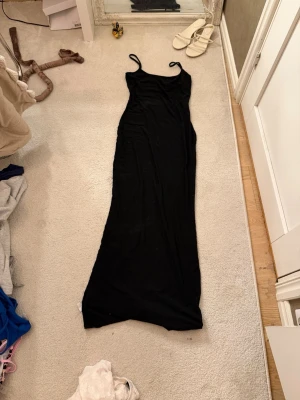 Svart långklänning med tunna band - Säljer en svart långklänning med tunna axelband. Klänningen har en enkel och stilren design som sitter snyggt längs kroppen. Perfekt för dig som gillar minimalistisk stil och vill ha något som alltid funkar. Shein!!