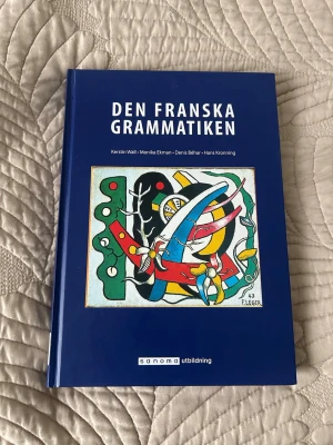 Den Franska Grammatiken bok - Blå kursbok i fransk grammatik med färgglad konst på omslaget. Skriven av Kerstin Wall, Monika Ekman, Denis Béhar och Hans Kronning. Perfekt för dig som pluggar franska och vill ha tydliga förklaringar och övningar.