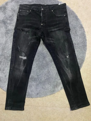Svarta skinny jeans från Dsquared2 - Säljer ett par svarta skinny jeans från Dsquared2 med slitningar och distressed detaljer på benen. Jeansen har klassisk femficksmodell, knappgylf och cool Dsquared2 patch bak. Tillverkade i Italien i mjukt jeansmaterial.