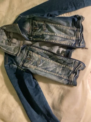 Blå jeansjacka med dragkedja - Säljer en klassisk blå jeansjacka från Cool Wear med dragkedja framtill och två bröstfickor med knappar. Jackan har långa ärmar och snygga sömdetaljer. Perfekt för dig som gillar en avslappnad och trendig stil.