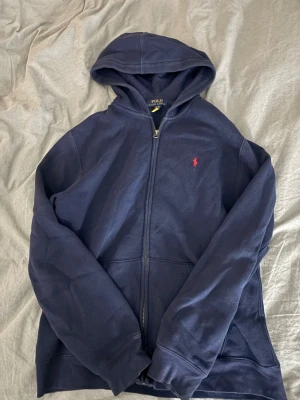 Polo Ralph Lauren - Jag säljer mitt mörk blåa mjukis sett, båda delarna är i storlek XL (6-14 Young). Byxornas midja band är snurrat, kan fixas. Även ett litet hål på byx benet som man inte tänker på, kan också sys ihop. Original pris för zip hoodie 1295kr och byxorna 1095kr.