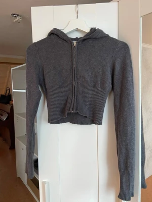 Grå cropped stickad hoodie - Säljer en grå stickad hoodie med dragkedja framtill. Tröjan är cropped och har långa ärmar med ribbstickade muddar samt huva. Perfekt för dig som gillar en avslappnad men trendig stil. Jätteskönt material. 🩷Strl 158/164 men passar XS-S