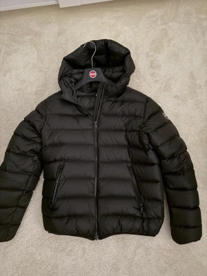 Svart dunjacka från Colmar med huva - Snygg svart dunjacka från Colmar med huva och två dragkedjeförsedda fickor. Jackan har quiltad design och en klassisk pufferlook som passar perfekt till kalla dagar. Dragkedja framtill och diskret logga på ärmen. OG MEDÖFLJER!!