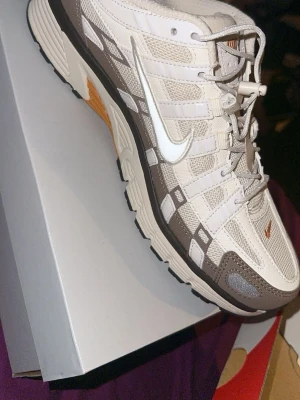 Nike P-6000 sneakers beige och brun - Nike P-6000 sneakers i beige och bruna toner med vita detaljer och meshpaneler. Skorna har en vit sula med svarta och orange inslag, samt klassisk Nike Swoosh på sidan. Designen är sportig med snörning och rund tå.