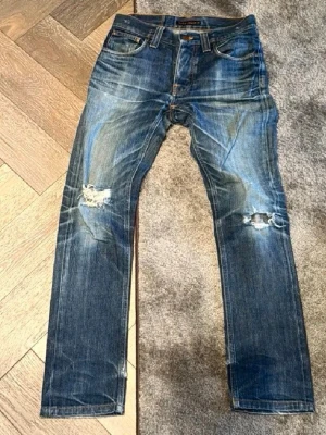 Nudie jeans grim tim - Säljer dessa feta nudie jeans i modellen grim tim!!! Dom har en skön fade och snygga slitningar. Skriv vid minsta fråga/fundering🙌🏼 Midja: 38,5 cm Innerbenslängd: 80 Benöppning: 17 cm