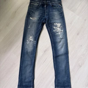 Blå Replay Grover jeans med slitningar - Säljer ett par blå Replay Grover jeans med snygga slitningar och tvättade detaljer. Klassisk femficksmodell med raka ben och normal passform. Perfekta för dig som gillar en avslappnad men stilren look.