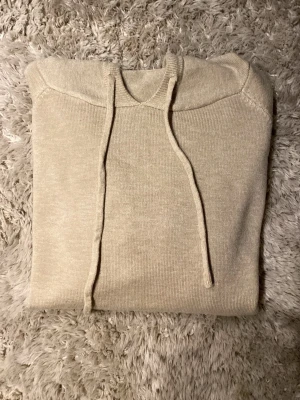 Beige Merinoull hoodie(Oanvänd) - Snygg beige hoodie med huva och snörning framtill. Tröjan har långa ärmar och ribbade muddar vid ärmslut och nederkant. Mjuk och skön, perfekt för chill dagar. Passar dig som gillar enkel och clean stil. Aldrig använd säljer för den är för liten för mig, Pris inte hugget i sten!!!
