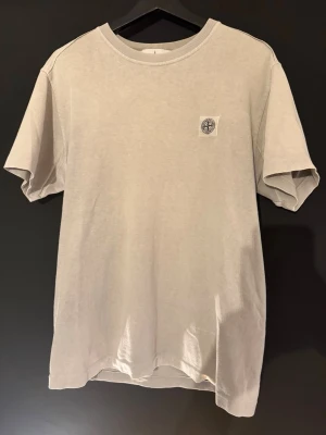 Stone Island t-shirt  - Snygg beige t-shirt från Stone Island med klassisk logopatch på bröstet. T-shirten har rund hals och korta ärmar, tillverkad i mjuk bomull, storlek M, fint skick, äkta såklart!
