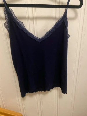 Mörkblå linnetopp med spets från newyorker  - Supersnygg mörkblå linnetopp från newyorker i storlek M. Toppen har tunna axelband och v-ringad hals med spetsdetaljer längs kanten. Materialet känns mjukt och lätt, perfekt för varma dagar. Enkel att matcha med jeans eller kjol för en chill look.