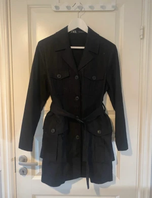 Trenchcoat klänning - Helt ny och oanvänd. Jätte fin trenchcoat som man även kan använda som klänning (tycker personligen den passar mer som klänning). 4 riktiga fickor fram och knäpps med knappar. Den formar kroppen fint och har skärp i midjan. Linne material så den är luftig och härlig. Passar även mig som brukar ha S.😊