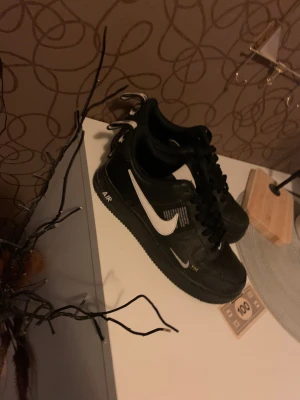 Nike Air Force 1 svart/vit sneakers - Svarta Nike Air Force 1 sneakers med vit swoosh och AIR-detalj på sulan. Skorna har snörning, platt sula och är tillverkade i skinn med textdetaljer på sidan. Väldigt unik Air force one skor som är svårt att få tag i idag