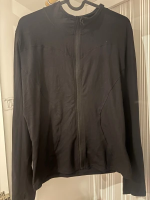 Svart långärmad zipjacka - Svart jacka med hel dragkedja framtill och lång ärm. Enkel och stilren design med smal krage, tillverkad i mjukt bomullsmaterial. Perfekt för dig som gillar minimalistisk look och vill ha något lätt att slänga på sig. Funkar till träning.