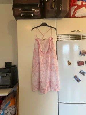 Rosa och vit sommarklänning med pärlor - Söt kortklänning i vitt och rosa med tunna axelband och korsad rygg. Klänningen har ett abstrakt mönster, pärldetaljer och vågig kant vid urringningen. Lätt och flowy modell, perfekt för varma dagar. Materialet känns som bomull eller syntet. Storlek M. Helt ny med tags/ prislapp fortfarande kvar. 