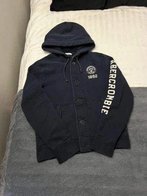 Abercrombie & Fitch Button Up Hoodie - Snygg och trendig Abercrombie kofta. Fint skick🙌. Storlek XL, men skulle säga att den sitter som en vanlig M (se mått nedan). Översta knappen är utbytt (knappt synligt) i övrigt perfekt. Perfekt julklapp nu till vinterkylan❄️  Längd från mitten på axel och ner: 66 cm Bredd under armhålorna: 53-54 cm Ärmlängd: 70 cm (mått nummer 2 på sista bilden)   Vänligen notera att måtten kan skilja 1-2 cm. Jag mäter alltid så noggrant som möjligt.