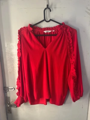 Röd Blus - Säljer denna jätte snygga och bekväma röda  blusen som har festliga detaljer så som voulanger på armarna och en liten v- ringning. Perfekt att ha på sig på julafton!