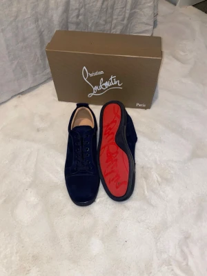 Mörkblå sneakers från Christian Louboutin - Snygga mörkblå sneakers från Christian Louboutin med klassisk röd sula och signatur på undersidan. Skorna har rund tå, snörning och är tillverkade i mocka med skinnfoder. Perfekt för dig som vill sticka ut med exklusiva detaljer och lyxig känsla.
