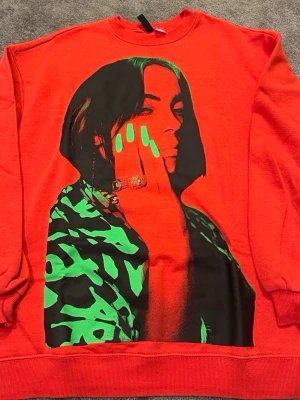 Röd sweatshirt med grafiskt tryck - Cool röd sweatshirt med ett stort grafiskt tryck på framsidan i svart och neon-grönt. Tröjan har rund hals och långa ärmar, perfekt för dig som gillar unika och färgstarka plagg. Materialet känns som mjuk bomull och passformen är normal.