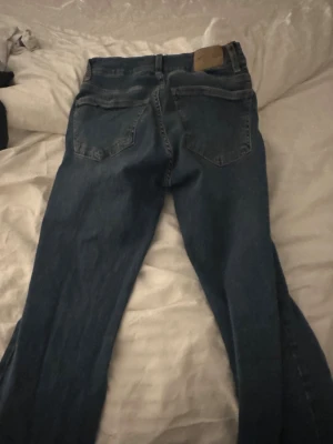Blå bootcut jeans från Gina Tricot - Snygga blå jeans från Gina Tricot, modell Perfect Jeans i storlek 36. De har klassisk femficksdesign, bootcut-ben och normal passform. Jeansen är tillverkade i jeansmaterial med en mörkblå tvätt och har en läderpatch bak i midjan.