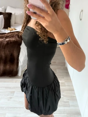 Svart axelbandslös kortklänning - Säljer en svart axelbandslös kortklänning med tight överdel och puffig, voluminös kjol. Sitter som en xs/s då tyget är stretchigt 