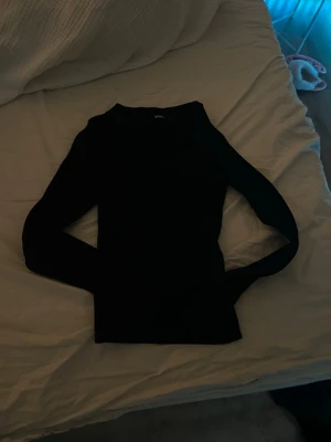 Svart långärmad tröja i bomull - En stilren svart långärmad tröja i mjuk bomull. Tröjan har en klassisk rund hals och en slim passform som sitter snyggt på kroppen. Perfekt att matcha med jeans eller kjol för en enkel och clean look.