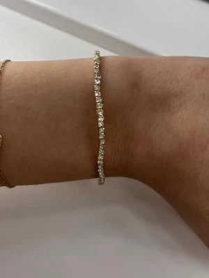 Glittrig guldfärgad armband - Säljer ett tunt guldfärgat armband med gnistrande stenar runt hela bandet. 💛 oanvänt! Köpte det när jag var i Spanien, så vet inte märket tyvärr.