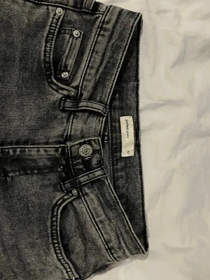 Svarta/mörkgrå bootcut jeans från Gina Tricot, perfect jeans - Jag säljer ett par svarta tvättade jeans från Gina Tricot i storlek 32. Modellen har bootcut-ben och klassisk femficksdesign. Jeansen är mid waist/high waist. Jeansen är i stretchigt denim och har en snygg, lite urtvättad stil. Längst ner på ena benet är de lite slitet (se bild) Innerbens längd 82cm Midjemått 71 cm