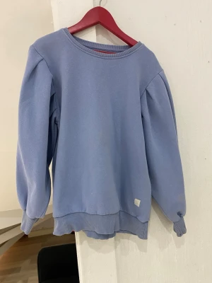 Ljusblå sweatshirt med puffärm - Säljer en ljusblå sweatshirt med puffade långärmar och ribbade muddar vid ärmslut och nederkant. Tröjan har en rund halsringning och är tillverkad i mjuk bomullsmix. Perfekt för dig som gillar stilrena och bekväma plagg med en twist.