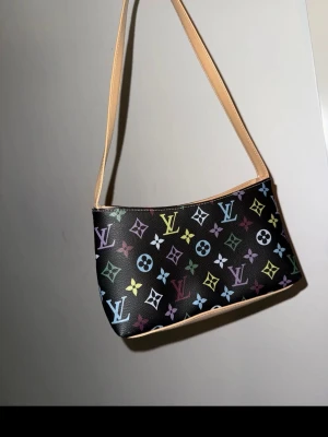  svart mönstrad lyxig axelväska med färgglatt mönster - Säljer en svart oanvänd mönstrad supersnygg handväska med ikoniskt mönster i flera färger som blått, gult, grönt, lila och rött. Väskan har beige axelrem och botten, samt dragkedja upptill. Perfekt storlek för det viktigaste och riktigt snygg att bära över axeln. Inga slitage eller något, 10/10.