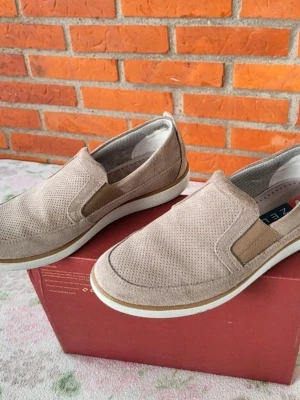 Beige mockaloafers från ZEUS Italy 41 passar 42 - Säljer ett par snygga loafers från ZEN i beige mocka med perforerat mönster och elastiska paneler på sidorna. Skorna har rund tå och vit platt sula med bruna detaljer. Perfekt för dig som gillar stilren och enkel design.