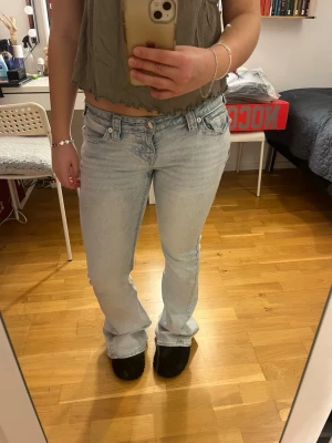 Ljusblå bootcut jeans från True Religion - Säljer ett par ljusblå jeans från True Religion med klassiska broderade fickor bak och snygga silverfärgade knappar. Modellen har bootcut och låg midja, tillverkade i mjukt denim-material. Perfekt för dig som gillar en chill och retro vibe.