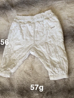 Vita broderade byxor från Newbie - Supersöta vita byxor från Newbie med broderade blommor och resår i midja och benslut. Perfekta för en gullig och bekväm stil till de allra minsta. Lätta och luftiga med fina detaljer som ger en extra touch.🌸 Fint använt skick. Storlek 56