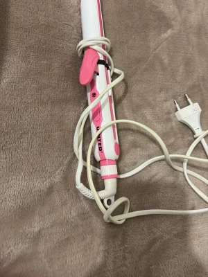 Rosa och vit locktång från United - Säljer en elektrisk locktång i rosa och vitt från United. Tången har ett handtag med rosa detaljer, en klämma för att hålla håret på plats och en lång vit sladd med EU-kontakt. Perfekt för att skapa snygga lockar och vågor.