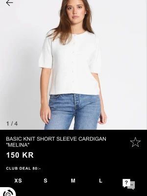 Vit stickad kofta med pärlknappar - Supersöt vit stickad kofta från Melina med korta ärmar och pärlknappar framtill. Koftan har en mjuk och fluffig känsla, rund halsringning och en clean look som passar perfekt till jeans eller kjol.