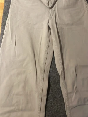 Beige chinos från Pull&Bear - Säljer ett par snygga beige chinos från Pull&Bear i storlek 38 EUR. Byxorna har klassisk passform med dragkedja och knapp framtill. Perfekta för dig som gillar stilrena och enkla byxor i bomull. Passar till många olika looks.