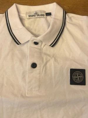 Vit Stone Island piké Medium - Säljer en vit pikétröja från Stone Island med svart broderad logga på bröstet. Passar Large Medium Small