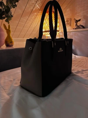 Svart handväska från Wittchen - Snygg svart handväska från Wittchen med stilrena guldiga detaljer och två rejäla handtag. Som ny! Andvänt få talls gånger❤️