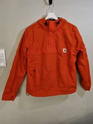 Carhartt allvädersjacka i storlek S/M - Säljer en Carhartt allvädersjacka i storlek M (men är mer som en S) som enbart blivit använd en gång.  Det är en W Nimbus Pullover i orange.  Inköpt för 1279:-, men säljer den för 700:-.  Jackans funktioner: - Fleecefodrad nylon Supplex® - Vattenavvisande Teflon-behandlat tyg - Fleecefoder - Justerbar huva och nederkant - Bröst- och sidofickor med dold dragkedja - Sidöppning med dragkedja  Finns i Hornstull i Stockholm!   Kan frakta, men då står köparen för frakten 😊 