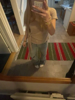 Beige omlottopp med knyt - Säljer en beige omlottopp med korta ärmar och snygg knytning i sidan. Toppen har en mjuk och enkel design som gör den lätt att matcha med olika stilar. Perfekt för dig som gillar neutrala färger och en chill look.