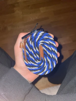 Blåvit flätad stretchbälte - Säljer ett snyggt flätat bälte i blått, vitt och svart med bruna skinn-detaljer och metallspänne. Bältet är elastiskt och passar perfekt till jeans eller chinos för en chill och stilren look. Ny pris 299kr.