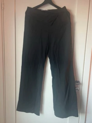 Svarta vida kostymbyxor - Säljer ett par svarta kostymbyxor med hög midja och vida ben. Byxorna har en snygg, enkel design utan synliga detaljer och är perfekta för en clean look. Tillverkade i ett mjukt och lätt material som känns skönt mot huden.