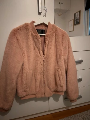 Ljusrosa teddyjacka från Bonprix - Mysig ljusrosa teddyjacka från Bonprix med dragkedja framtill och ribbade muddar. Jackan har en fluffig yta och två fickor på sidorna. Perfekt för dig som vill ha en trendig och varm jacka med skön passform.