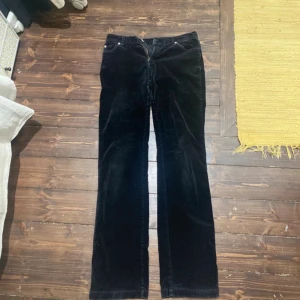 Svarta manchesterbyxor bootcut - Säljer ett par svarta manchesterbyxor med bootcut-snitt. Byxorna har klassisk femficksdesign och dragkedja fram. Perfekta för dig som gillar retrovibbar och vill ha ett par byxor som sticker ut lite extra.