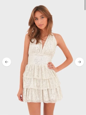 Paljett klänning  - Supersnygg klänning med paljetter och volanger. Klänningen har halterneck, öppen rygg och markerad midja. Perfekt för dig som vill sticka ut och glänsa! Klänningen är helt ny med prislapp på, säljer då den inte passade. Nypris:600kr 