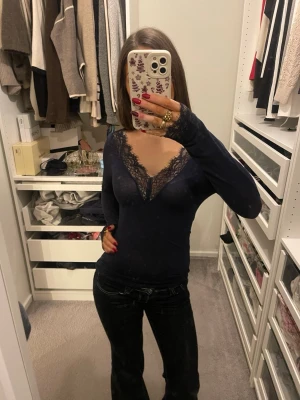 Blå långärmad topp med spets Intimissimi - Mörkblå långärmad topp från Intimissimi med v-ringning och fina spetsdetaljer vid halsringning och ärmslut. Tunn och mjuk, perfekt att styla med jeans eller kjol. Snygg och feminin look med en touch av elegans.