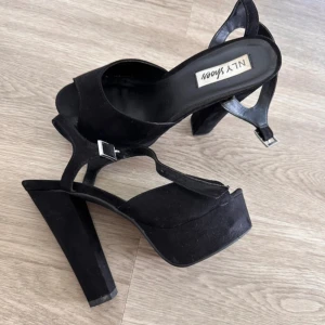 Svarta platåsandaler från NLY Shoes - •Säljer ett par svarta högklackade sandaler med en platåsula & klack på 14 cm från NLY Shoes. •Skorna har öppen tå, justerbart spänne vid ankeln och breda remmar. Det finns har några små men diskreta skador på mockan vid klacken (se sista bilden) men i övrigt är de i jättefint skick. Kan skicka flera bilder vid behov.