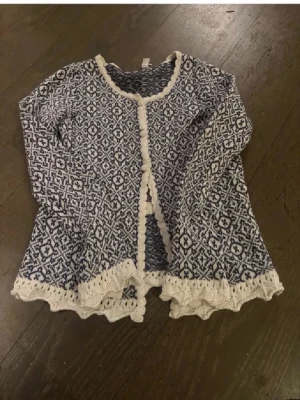 Blåvit mönstrad kofta med spetskant - Supersöt kofta från Resebud i blått och vitt med ett detaljerat mönster. Koftan har lång ärm, rund hals och knappar framtill. Spetskant i vitt längs nederkant, ärmslut och halsringning ger en extra touch. Perfekt för dig som gillar unika plagg med vintagekänsla. Använd gärna köp nu❤️