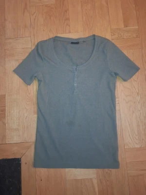 Grön kortärmad topp med knappar - Säljer en enkel grön topp med korta ärmar och rund halsringning. Toppen har en knappdetalj framtill med fyra små knappar. Materialet känns mjukt och stretchigt, perfekt för en chill stil. Bara använd ett fåtal gånger, så väldigt bra kvalitet! 